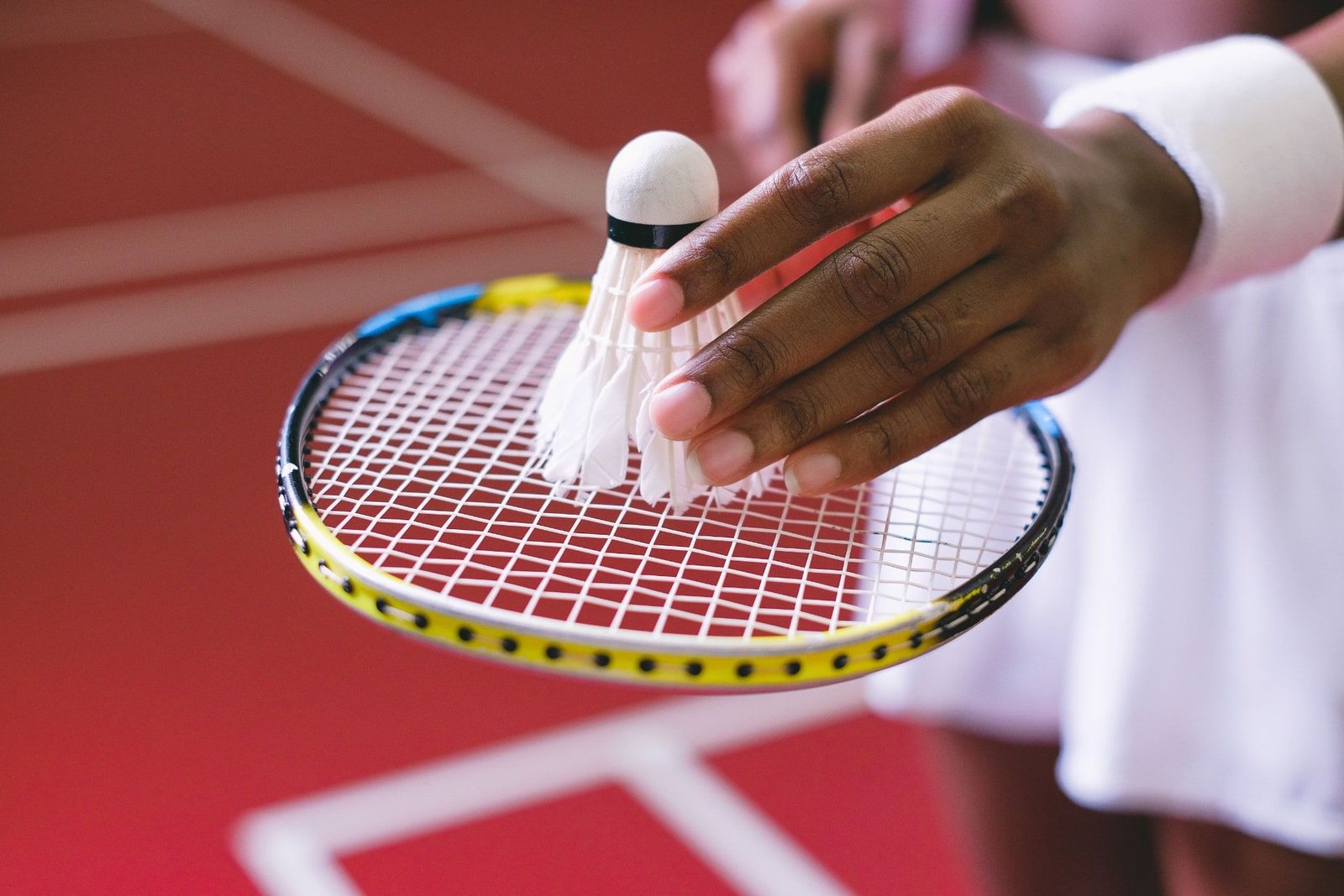 Hand holding a badminton racquet and shuttlecock over a red court. Not the Sector 92 project.