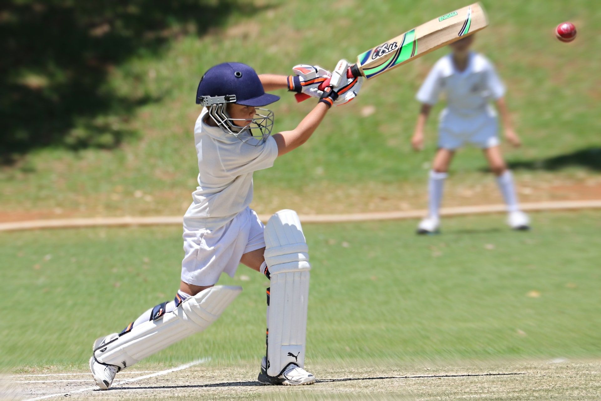 Young batter playing a shot on a grass cricket ground. Not the Sector 92 project.